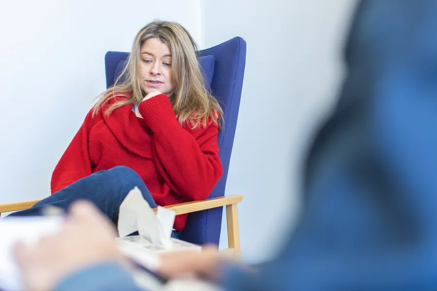 En kvinne med rød genser som sitter i en stol med tørkepapir i hånda.