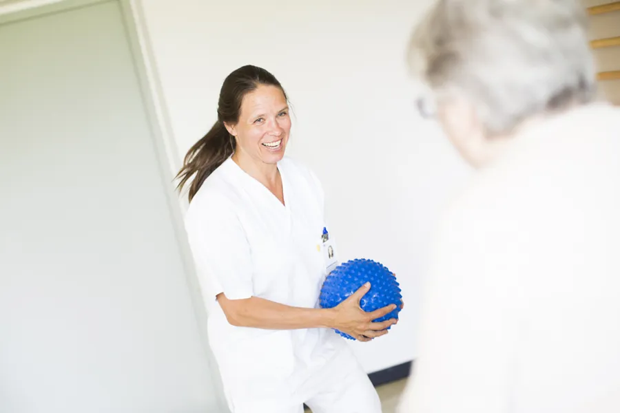 En kvinnelig sykepleier med fysioterapiball snakker med kvinnelig pasient.