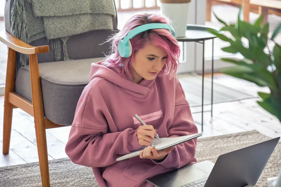 Jente med rosa hår foran laptop.